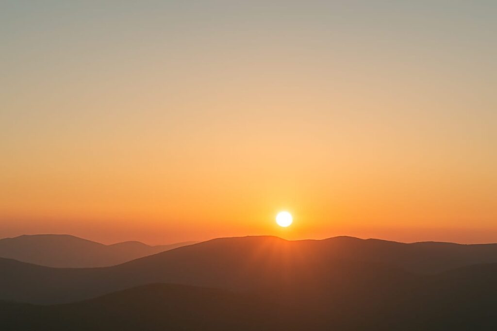A digital illustration of a sunrise over a serene mountain landscape, with warm golden light illuminating the sky and gentle mist drifting through the valley below.