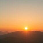 A digital illustration of a sunrise over a serene mountain landscape, with warm golden light illuminating the sky and gentle mist drifting through the valley below.